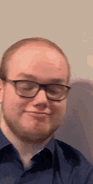 a man wearing glasses and a blue shirt looks at the camera