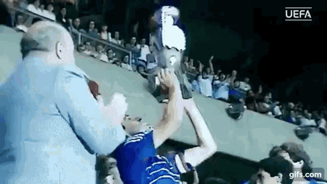 a man in a blue shirt is holding a trophy in a crowd of people .