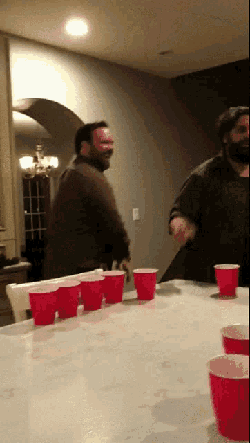 two men are playing a game of beer pong with red cups