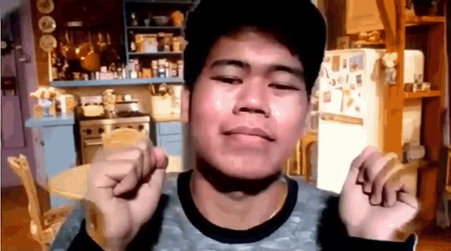 a young man is making a funny face in a kitchen with a refrigerator in the background .
