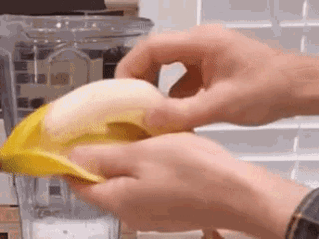 a person is peeling a banana and putting it into a blender .