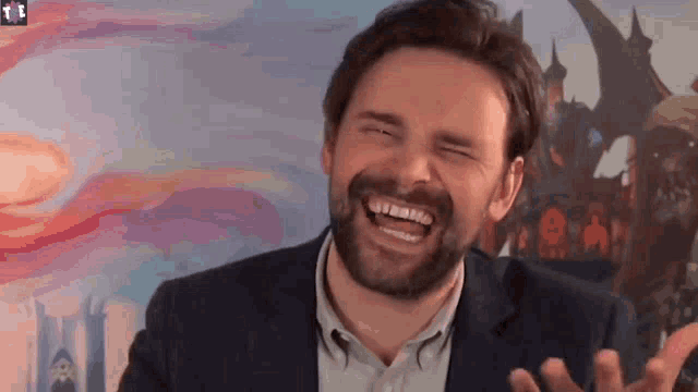 a man with a beard is laughing with his eyes closed in front of a castle .