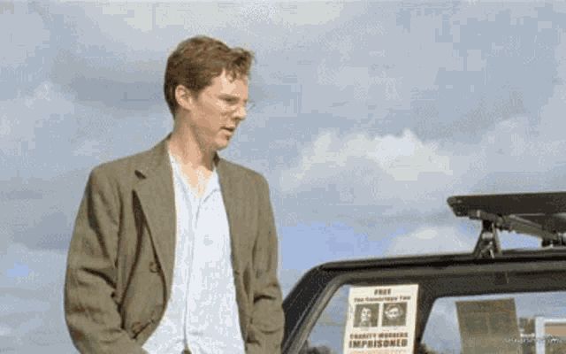 a man in a suit is standing next to a car with a sign on the roof that says free charity work for imprisoned