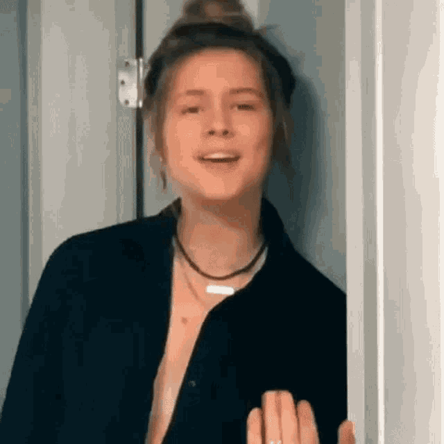 a woman wearing a black shirt and a necklace is standing in a doorway .