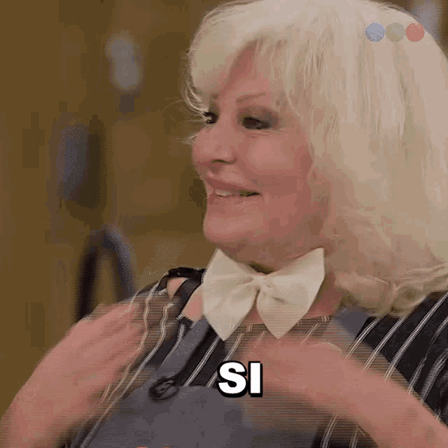 a woman with white hair and a bow tie is smiling and says si .