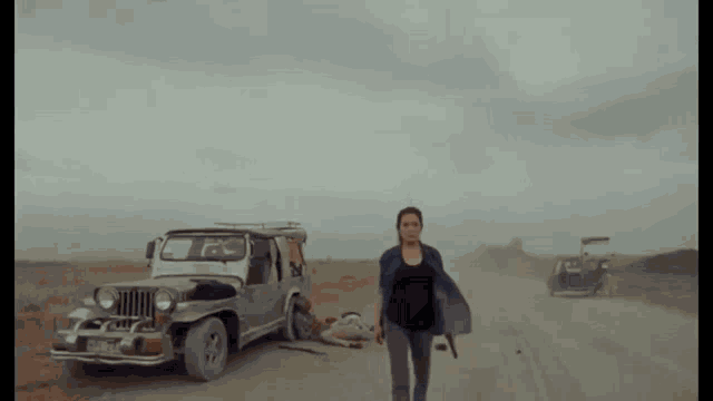 a woman is walking down a dirt road in front of a jeep .