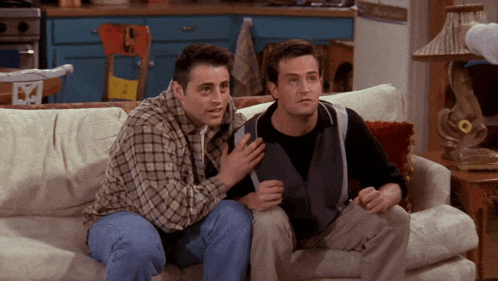 two men are sitting on a couch and one has his hand on the chest of the other