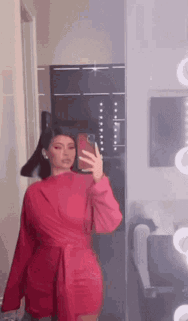 a woman in a red dress is taking a picture of herself in the mirror .