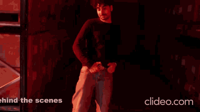 a man is standing in a dark room with the words behind the scenes on the bottom right