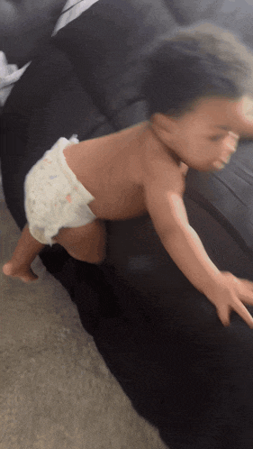 a baby wearing a diaper is crawling on a black couch