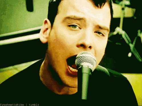a close up of a man singing into a microphone with tumblr written on the bottom right