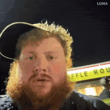 a man with a beard wearing a hat is standing in front of a waffle house