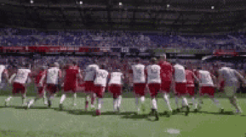 a group of soccer players are running on the field holding hands .