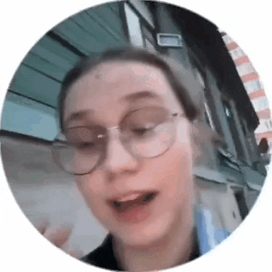 a woman wearing glasses is standing in front of a building and making a funny face .