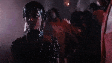 a woman in a black dress is surrounded by a group of people covered in red paint .