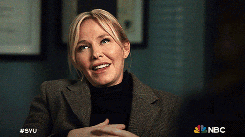 a woman in a suit and black turtleneck is smiling with the nbc logo behind her