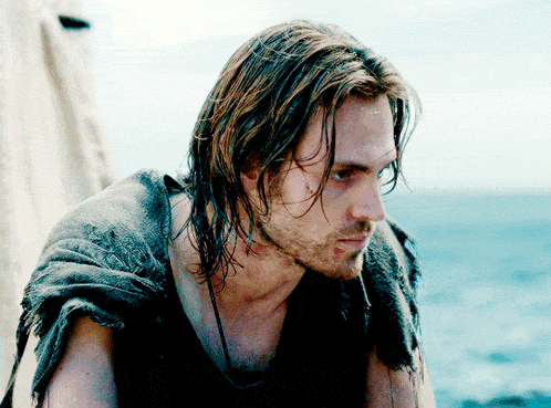a man with long hair and a beard is standing in front of a body of water
