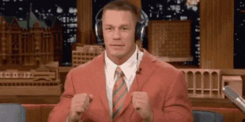 a man in a red suit and tie is wearing headphones and making a fist .