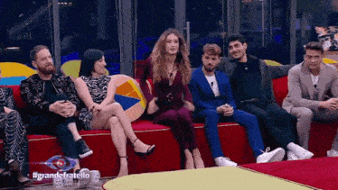 a group of people are sitting on a red couch with the words grande fratello on the bottom