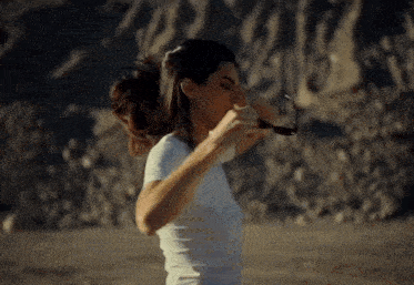 a woman in a white t-shirt is holding a pair of sunglasses in her hand