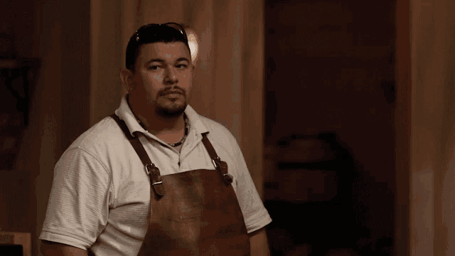 a man wearing a white shirt and a brown apron looks at the camera
