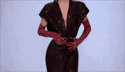 a woman in a black jumpsuit and red gloves is standing on a white background .