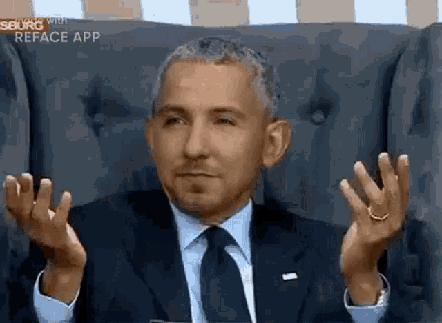 a man in a suit and tie is sitting in a chair with his hands up in the air .
