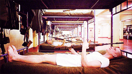 a man in a white shirt is laying on a bunk bed with a gun in his hand