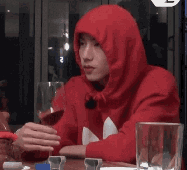 a man wearing a red hoodie is holding a glass of wine