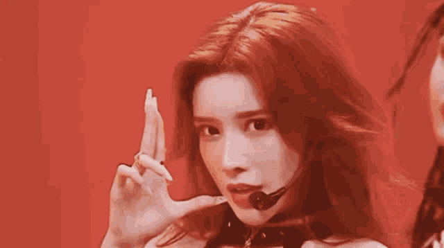 a woman wearing a choker and a microphone is smiling and making a peace sign .