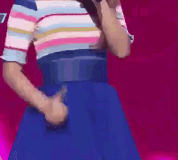 a woman in a striped shirt and blue skirt is singing into a microphone