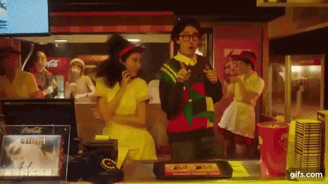a man in a red and green sweater is standing in front of a counter in a fast food restaurant .