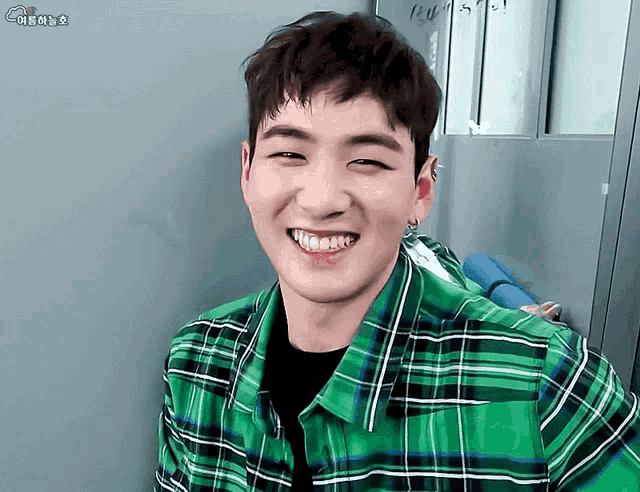 a young man wearing a green plaid shirt smiles
