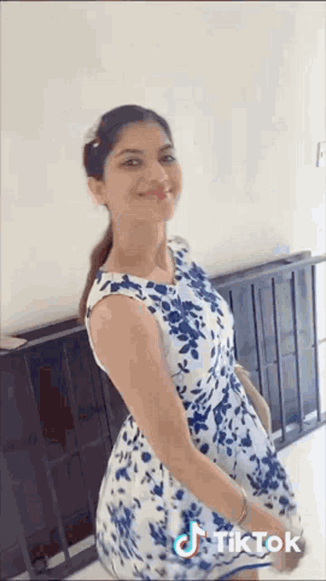 a woman in a blue and white floral dress is standing in front of a railing .