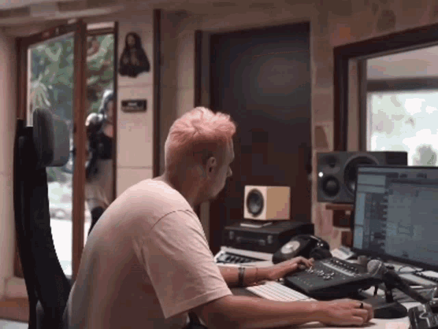 a man with pink hair is sitting at a desk in front of a computer monitor