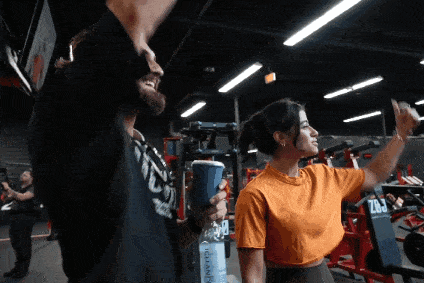 a man and a woman are standing in a gym and the man is wearing a black shirt that says ufc on it