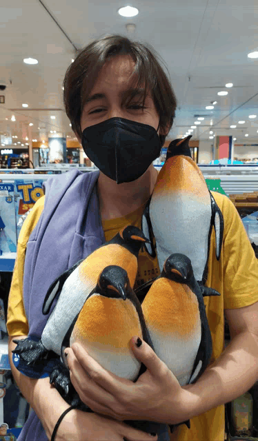 a man wearing a mask is holding three stuffed penguins in his arms