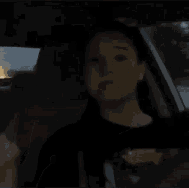 a young boy is sitting in the driver 's seat of a car in the dark .