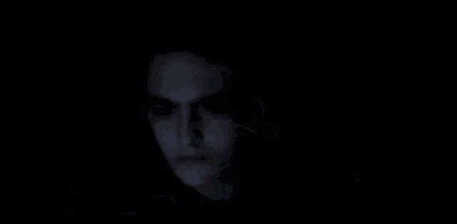 a man in a black shirt is holding his head in the dark .