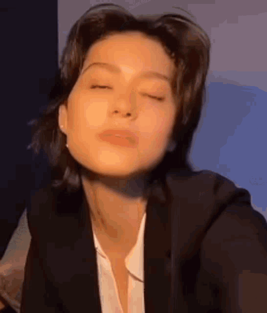 a close up of a woman wearing a suit and a white shirt with her eyes closed .