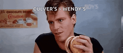 a man is holding a hamburger in his hand in front of a sign that says culver 's > wendy 's