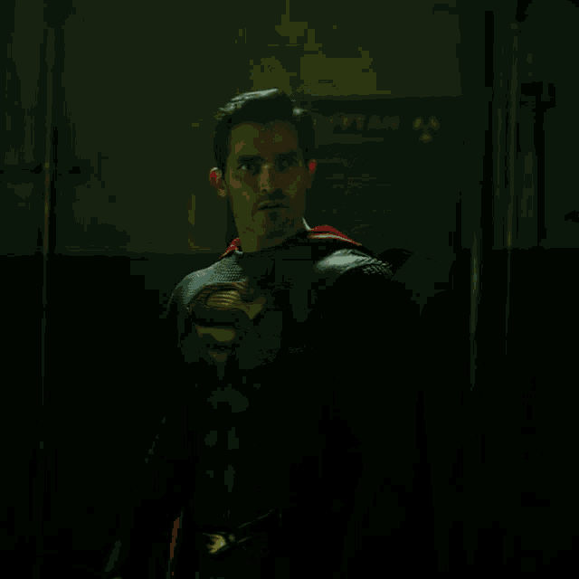 a man in a superman costume with the letter s on his chest stands in a dark room