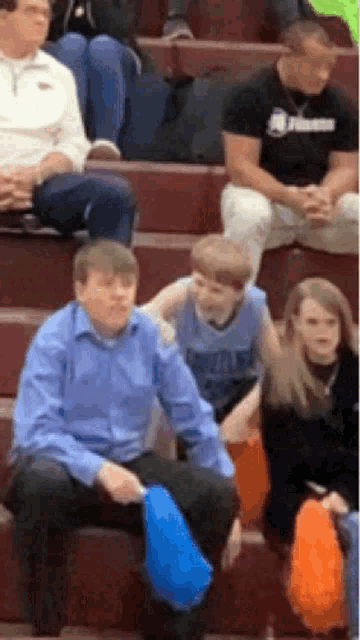 a group of people are sitting in a stadium watching a game and one of them is holding a blue fan .