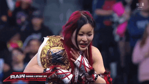a woman with red hair is holding a wrestling championship belt in front of the raw logo