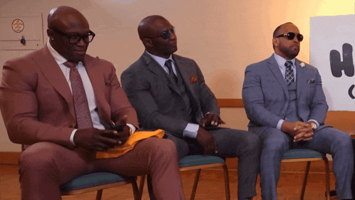 three men in suits sit in chairs in front of a sign that says " no smoking "