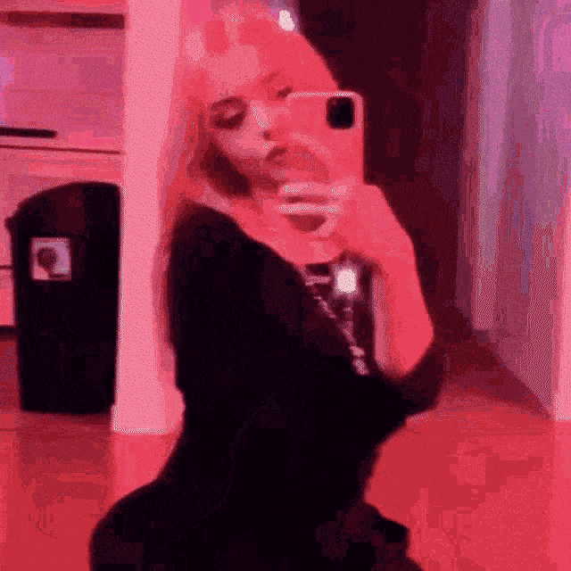 a woman is taking a picture of herself in a mirror with a pink background .