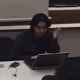 a man is sitting at a table with a laptop and smoking a cigarette .