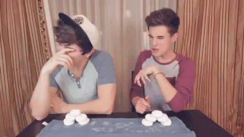 two young men are sitting at a table with marshmallows