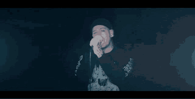 a man is singing into a microphone in the dark while wearing a hat .