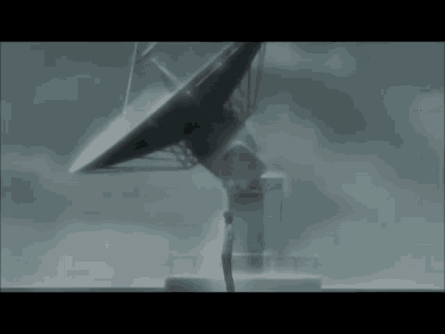 a man is standing in front of a large satellite dish on a cloudy day .